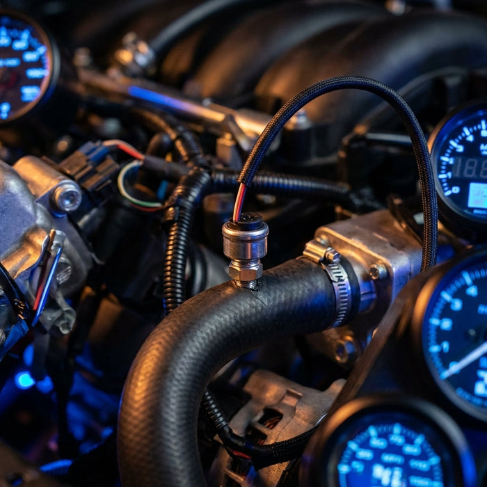 Creative rendering of a compact fuel and oil pressure sensor installed in a rubber hose, featuring ambient lighting and engine background elements.