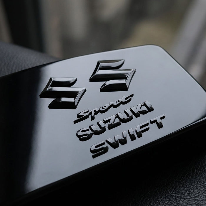 Micro-focused shot of a 5-piece glossy black Suzuki Swift Sport emblems set highlighting high-polish finish and intricate engraved details on reflective surface.