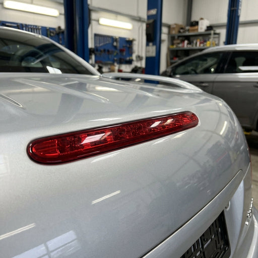 Close-up of a compact red LED brake light with textured lens on Peugeot 206cc trunk in a professional workshop.